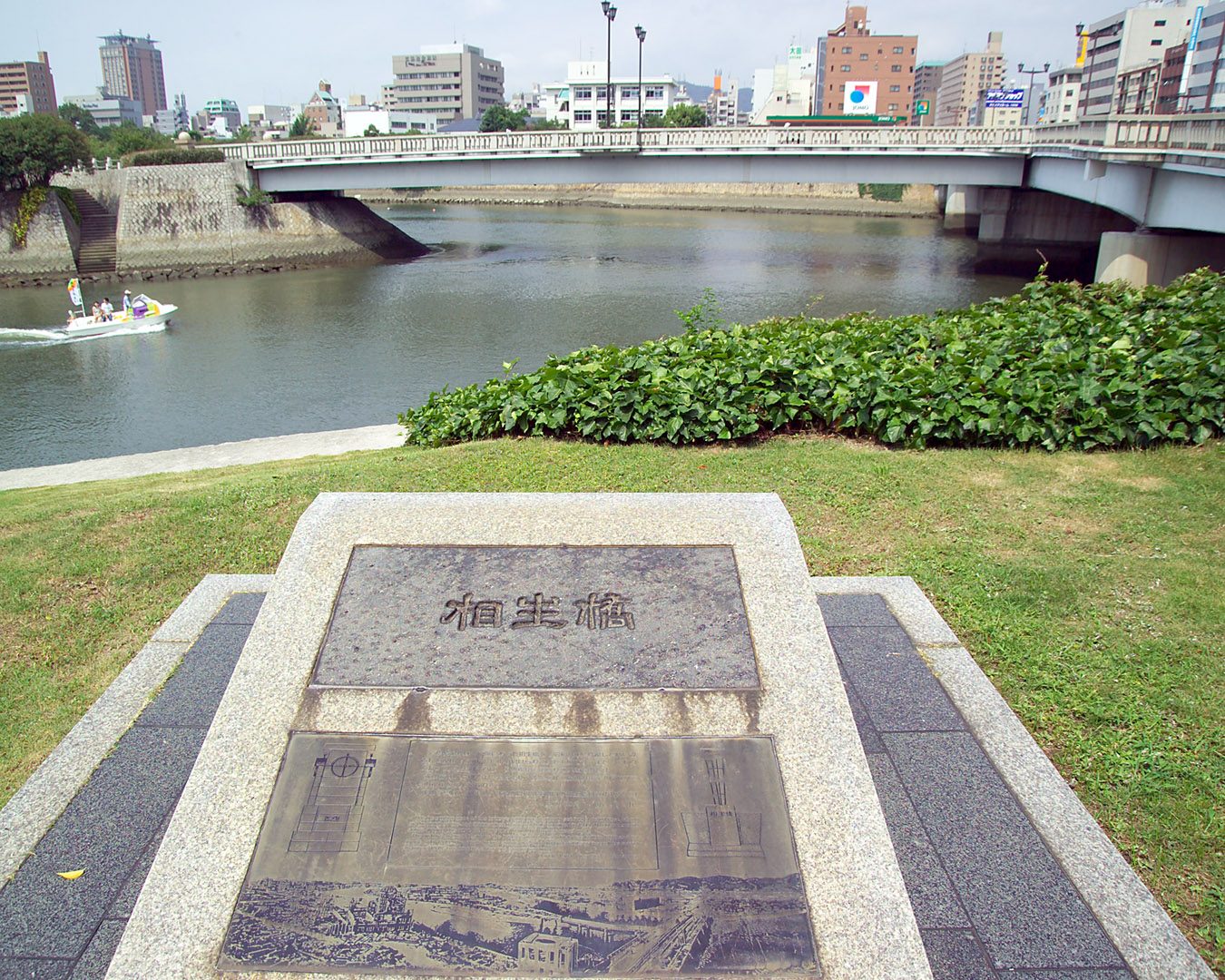A stone marker for Aioi Bridge on the riverbank in Hiroshima, with the bridge behind