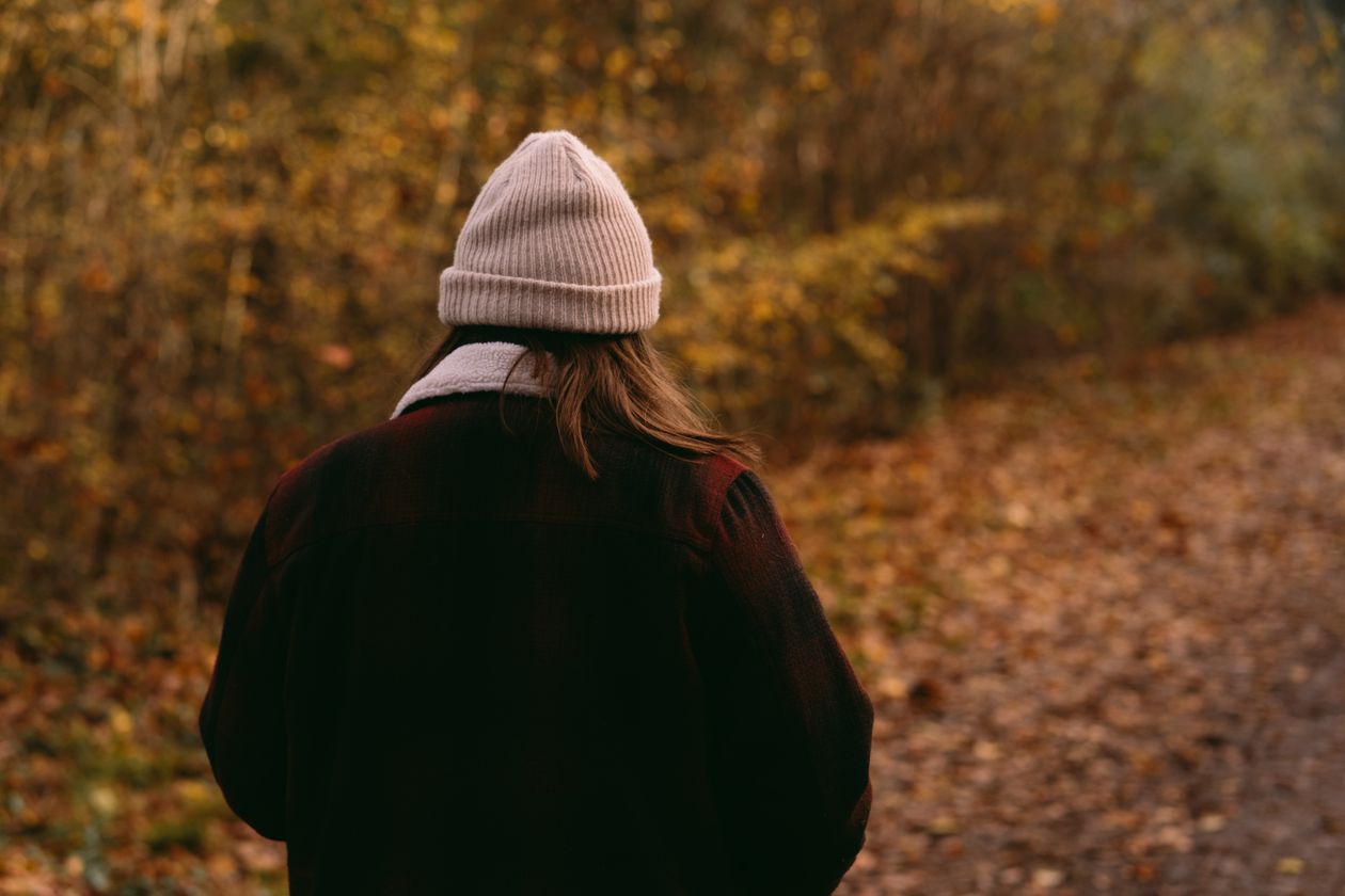 A woman in a knitted hat walking on an autumn path