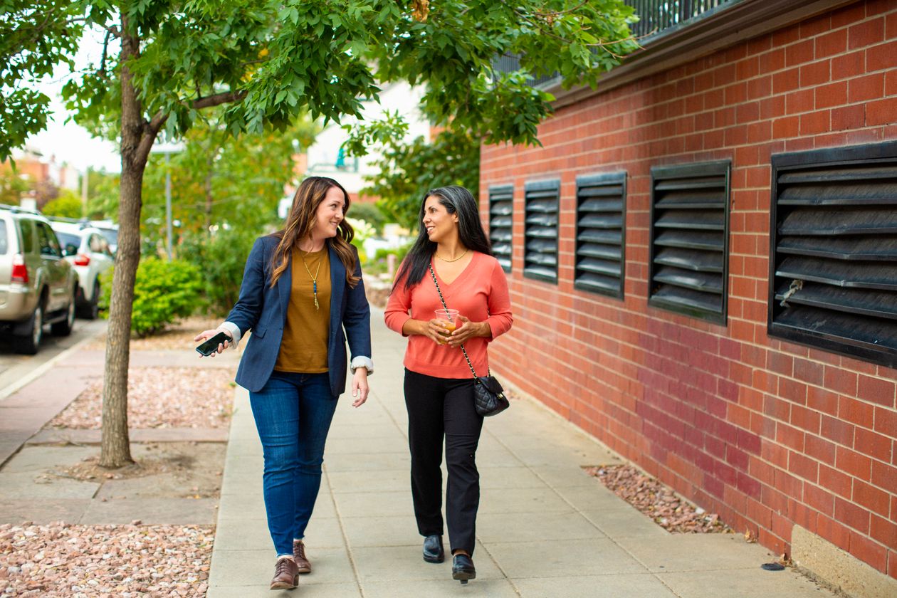 Two friends chatting as they walk along a pavement